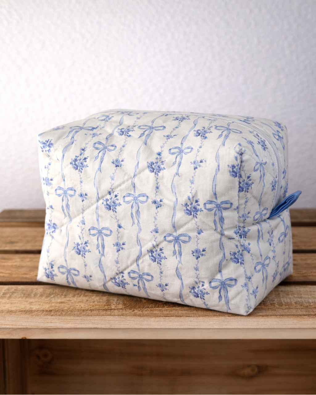 Boxed quilted cosmetic bag with blue floral pattern on a wooden surface
