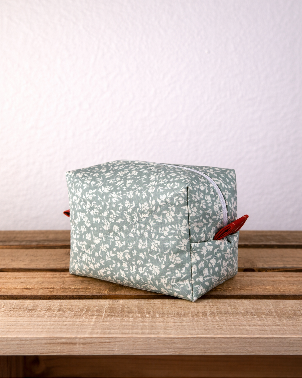 Green floral-patterned cube-shaped pouch on a wooden surface with a white background