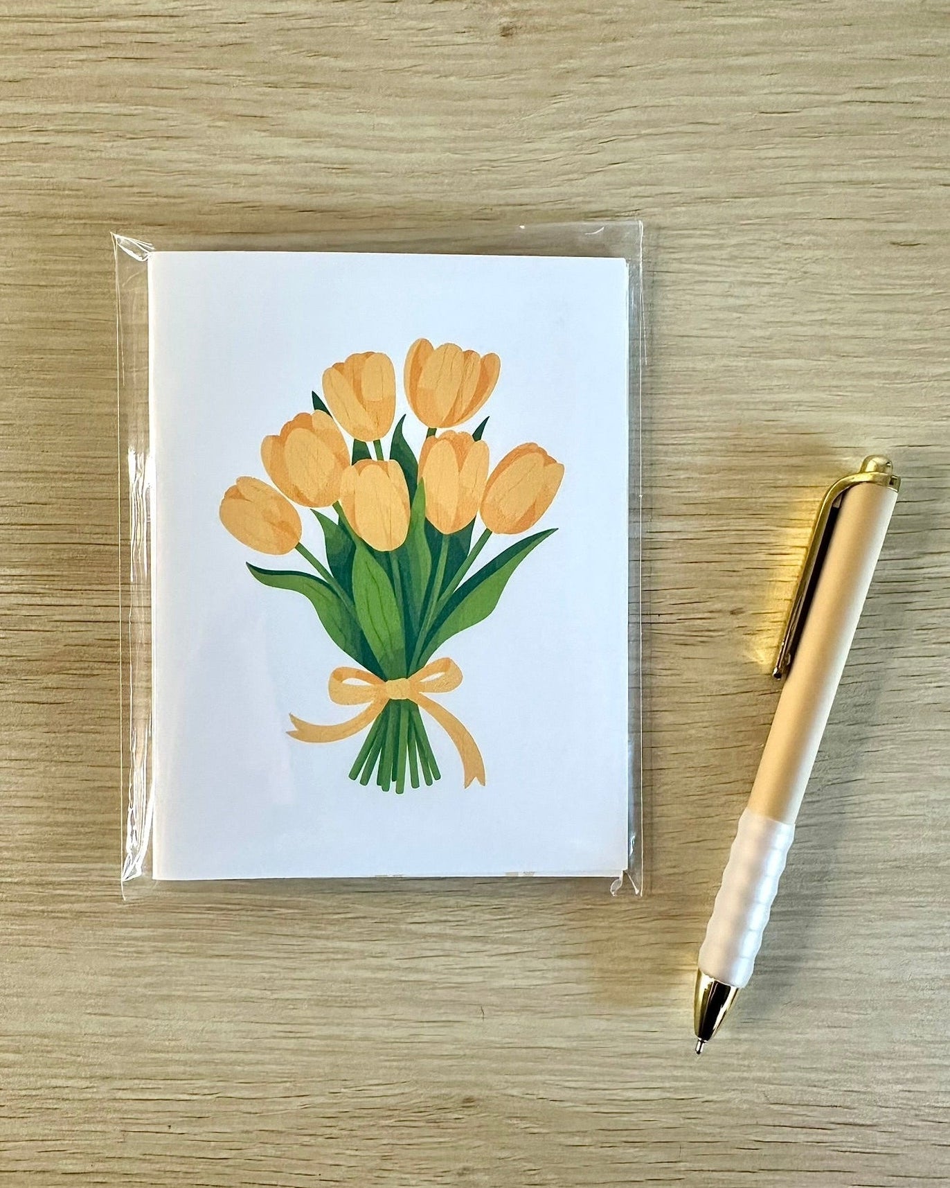 Greeting card with yellow tulips design on a wooden surface with a pen.