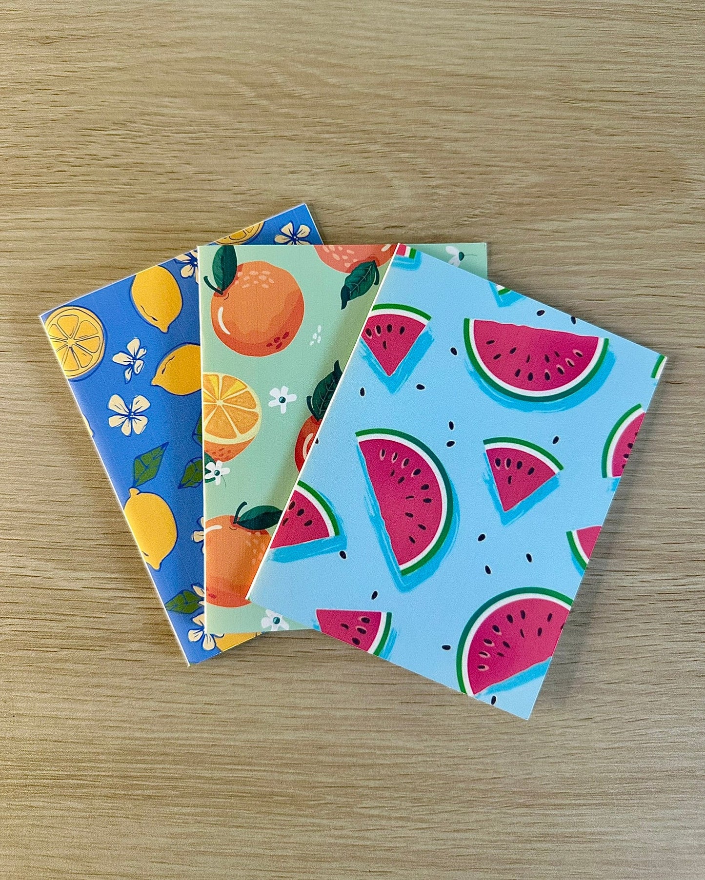 Three colorful greeting cards with fruit patterns on a wooden surface