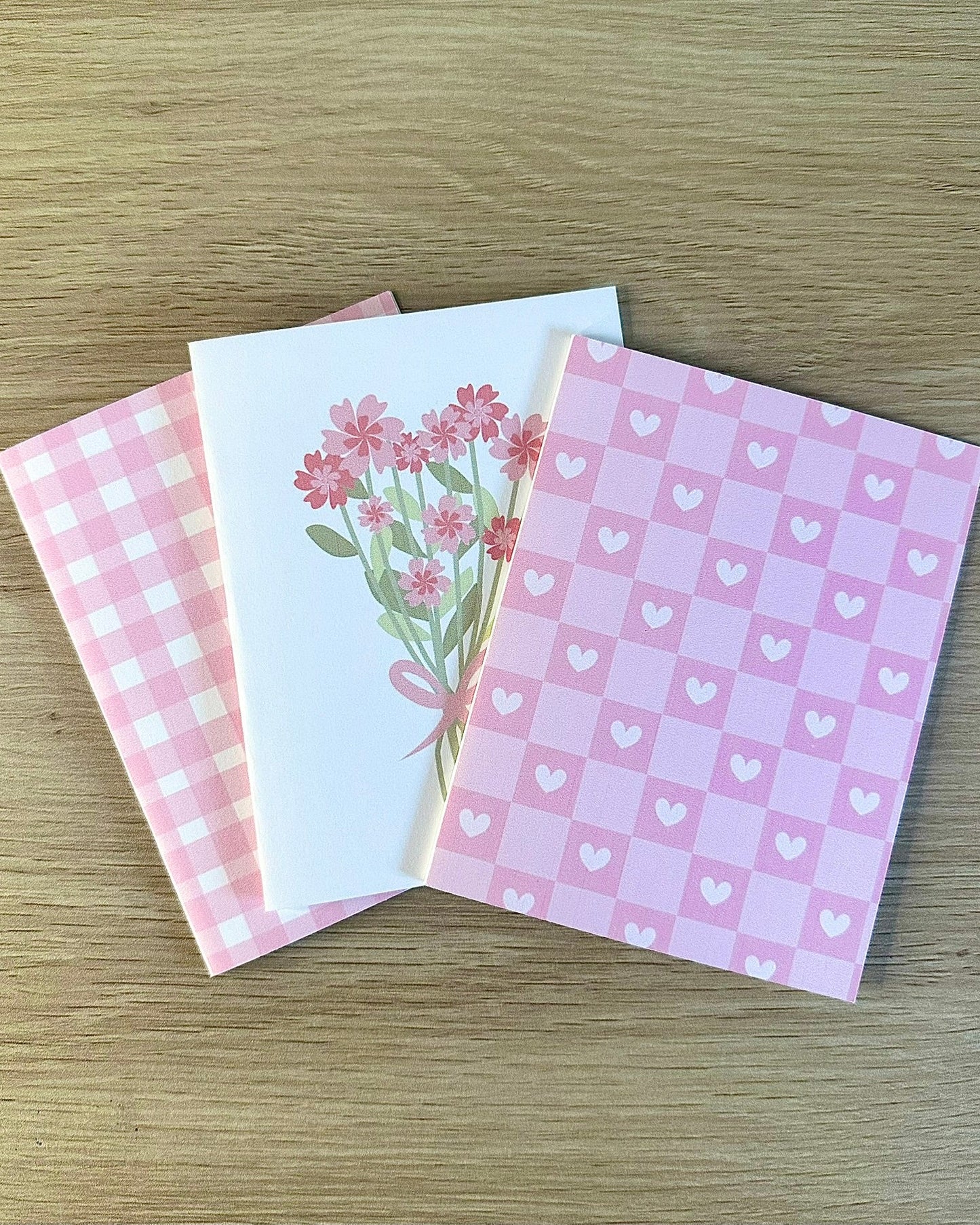 Three pink patterned greeting cards on a wooden surface
